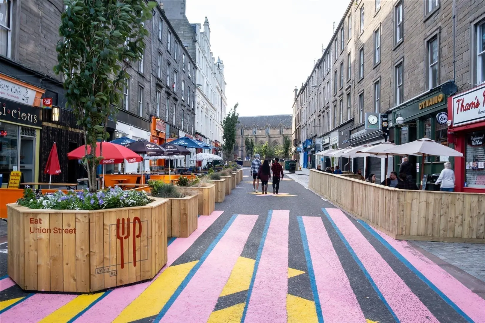 View of Union Street from the south end looking north up the street with pink, blue and yellow rectangles painted onto the floor in the foreground and wooden seats and planters bringing colour to the street