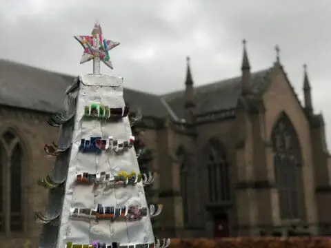 Tip of a 2022 christmas tree covered in cut up drinks cans which are curling up like tree branches, City Churches in the background blurry